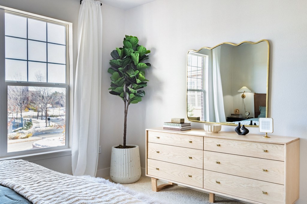 A bedroom with a large window, a white dresser, and a mirror. at The Viridian Apartments, Greenwood Village, CO