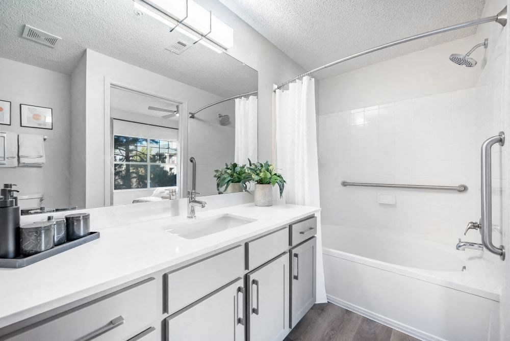 A white bathroom with a sink, mirror, and bathtub.