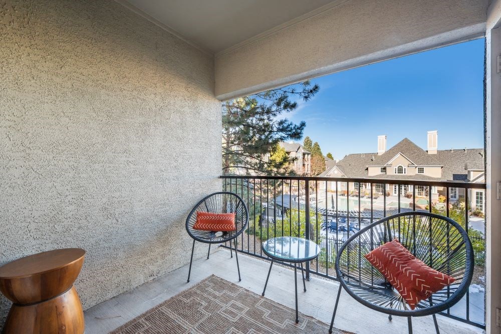 A balcony with a chair and a table with a red pillow.