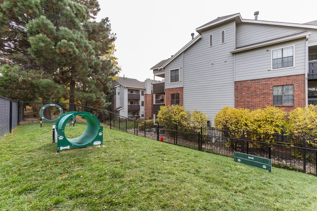 A playground with a green slide in front of a grey building.