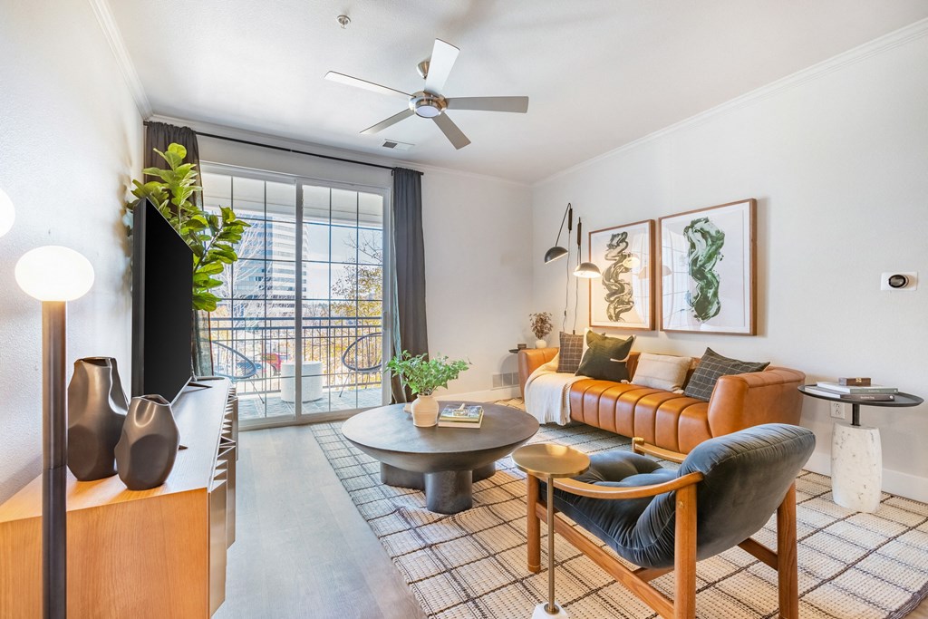 A living room with a brown couch, a grey armchair, a coffee table, and a ceiling fan. at The Viridian Apartments, Greenwood Village