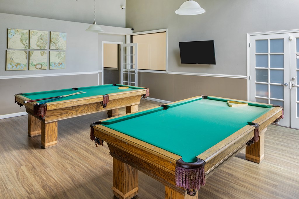 Two pool tables in a room with a door and a window.