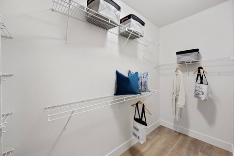 a spacious closet with white walls and shelves and bags hanging on the wall