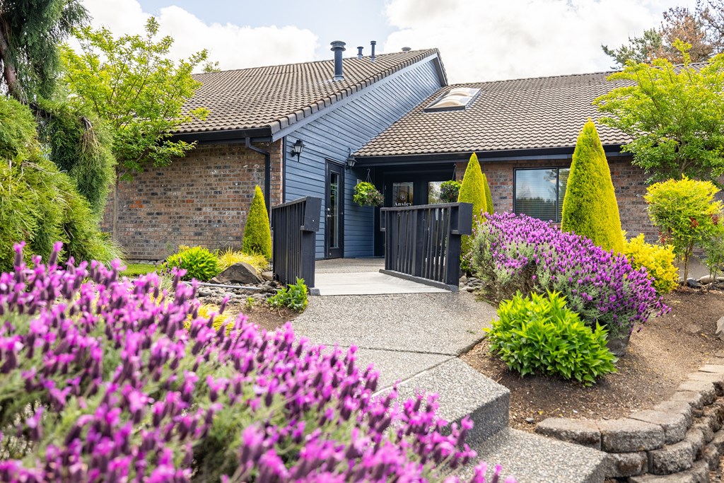 A house with a grey roof and a garden with purple flowers in front.