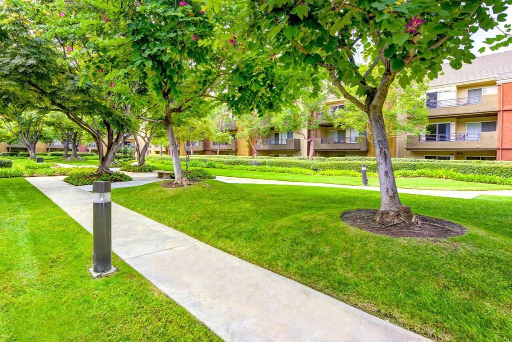 a sidewalk through a green park in front of an apartment building