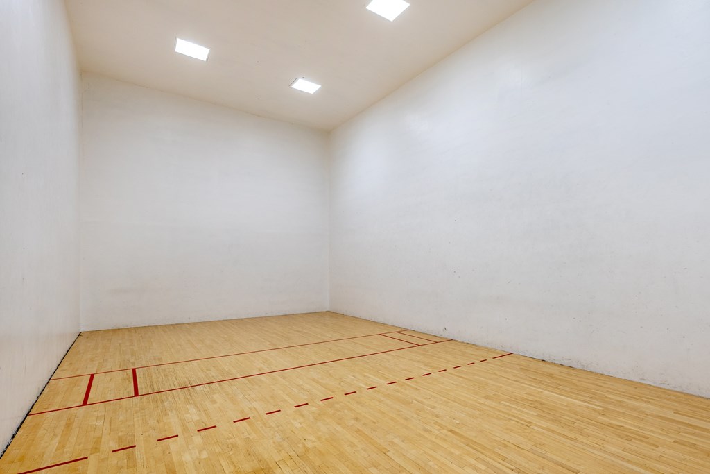 A squash court with a wooden floor and white walls.