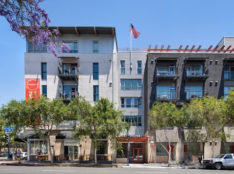 A modern building with a flag on top and a red sign on the left side.