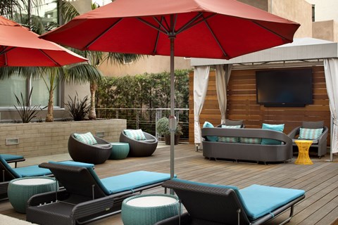 A red umbrella is in the middle of a set of wicker chairs and tables.