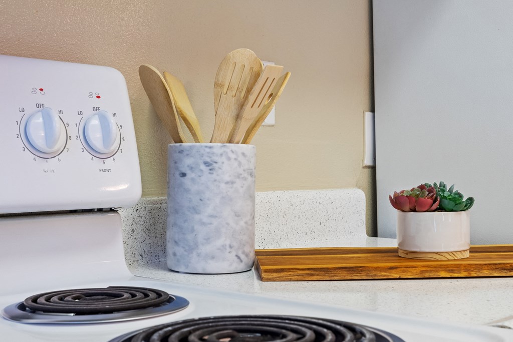 a kitchen counter with a stove and a vase with wooden utensils