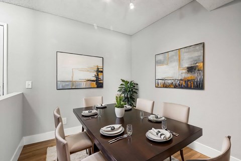 A dining room with a table set for two and two framed pictures on the wall.