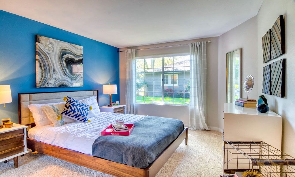 a bedroom with a bed and a blue wall and a window