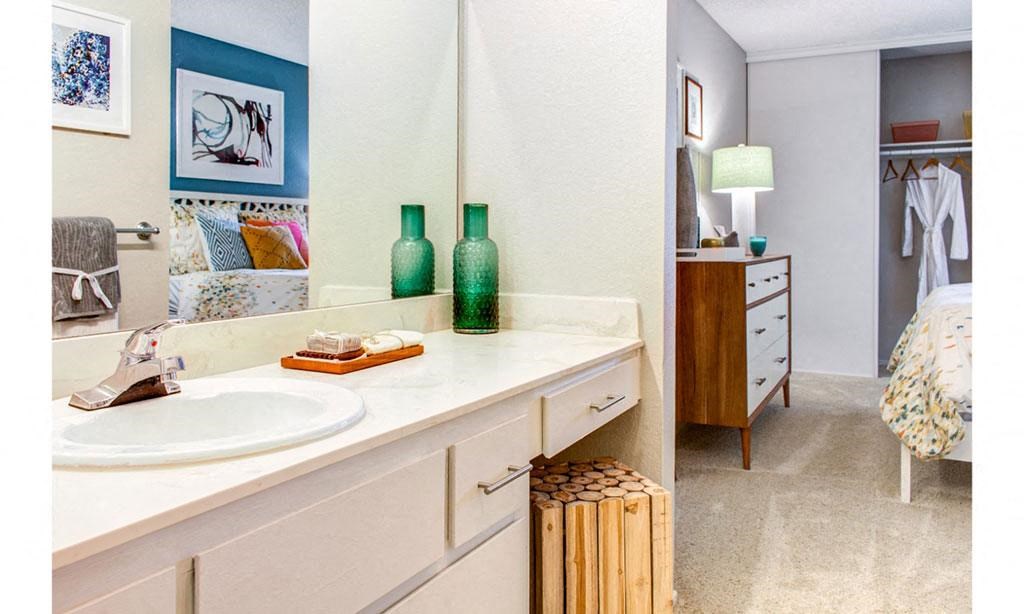 a bathroom with a sink and a mirror and a bedroom