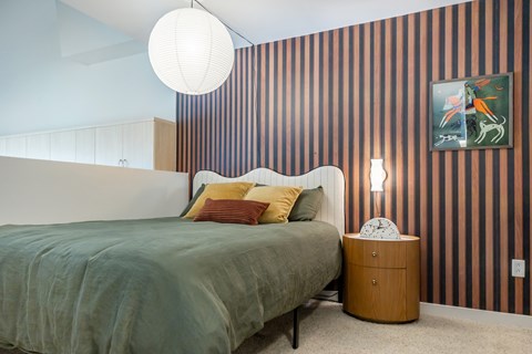 A bedroom with a bed, a side table, and a painting on the wall.