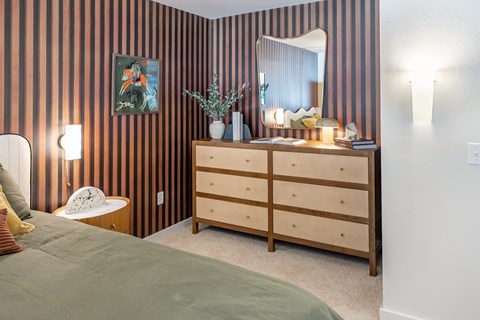 A bedroom with a striped wallpaper and a wooden dresser.
