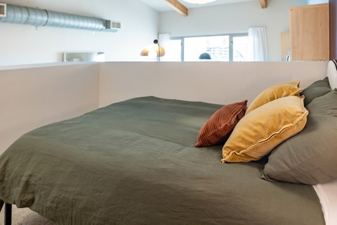 A bed with a green cover and two pillows in a room.