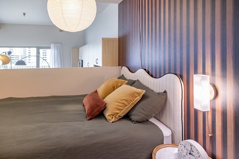A bed with a grey blanket and pillows is in front of a striped wall.