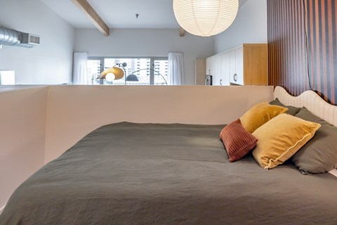 A bed with a grey cover and two pillows in a room with a window.