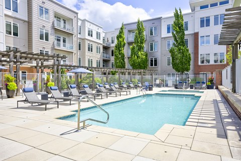 A pool surrounded by chairs and trees in a courtyard.
