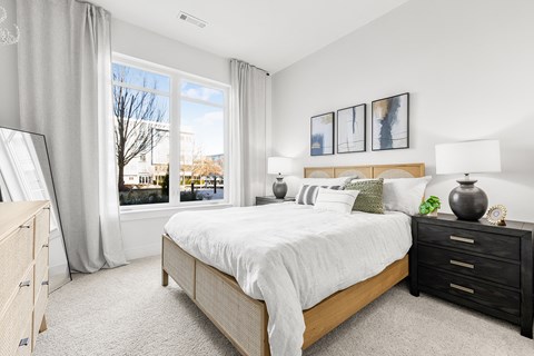 A bedroom with a large bed, a nightstand, and a window with a view of the city.
