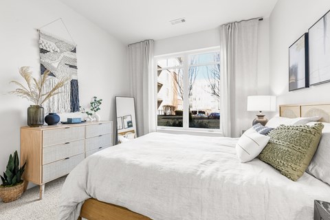 A bedroom with a large bed, a wooden dresser, and a potted plant.