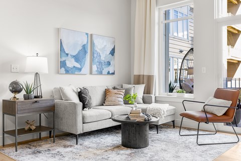 A living room with a grey couch, a brown chair, and a painting on the wall.