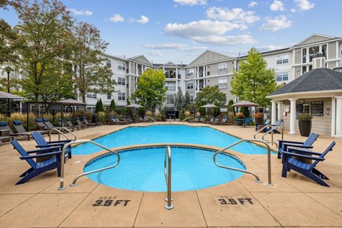 A large swimming pool surrounded by blue lounge chairs and apartment buildings in the background.