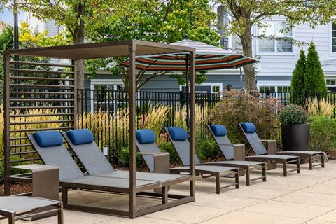 A row of blue lounge chairs are arranged under a striped umbrella.
