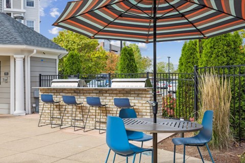 A patio with blue chairs and a striped umbrella.