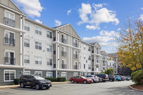 A row of apartment buildings with cars parked in front.