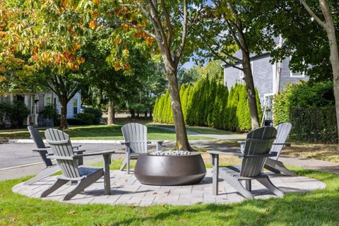 A set of chairs and a table are arranged around a fire pit in a garden.