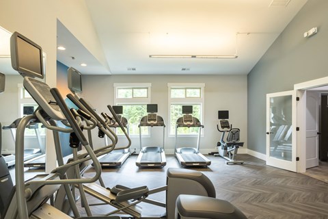 a gym with various cardio machines and windows