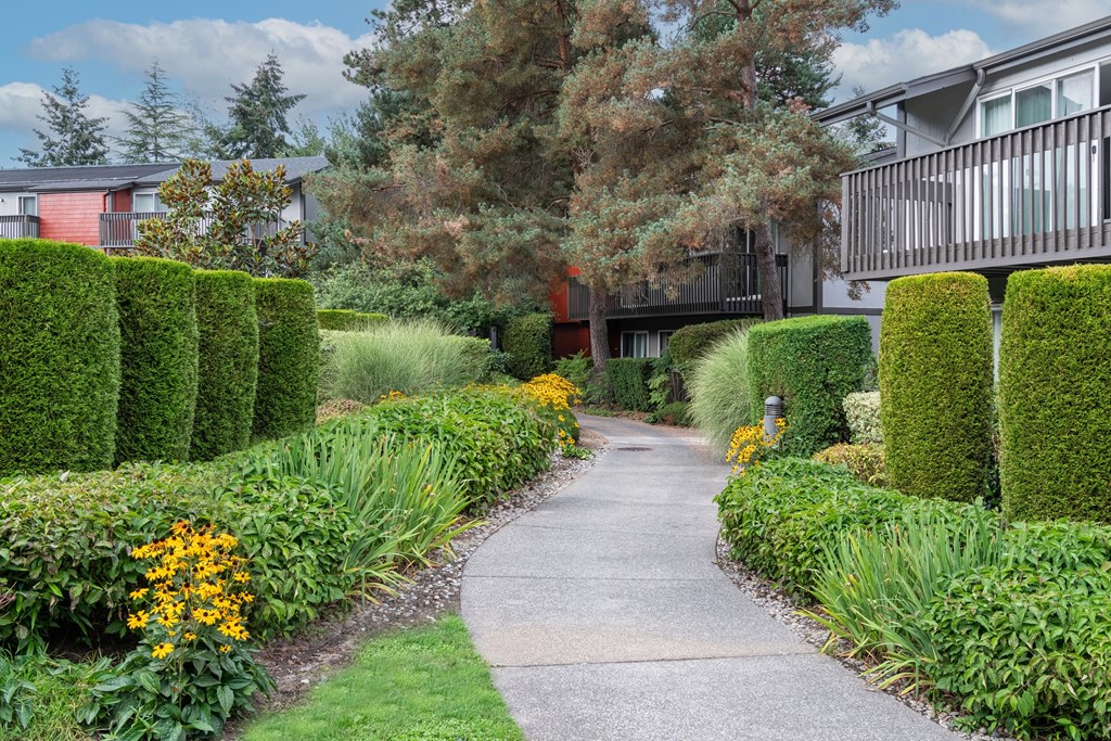 A pathway leads through a well-manicured garden with a building in the background.
