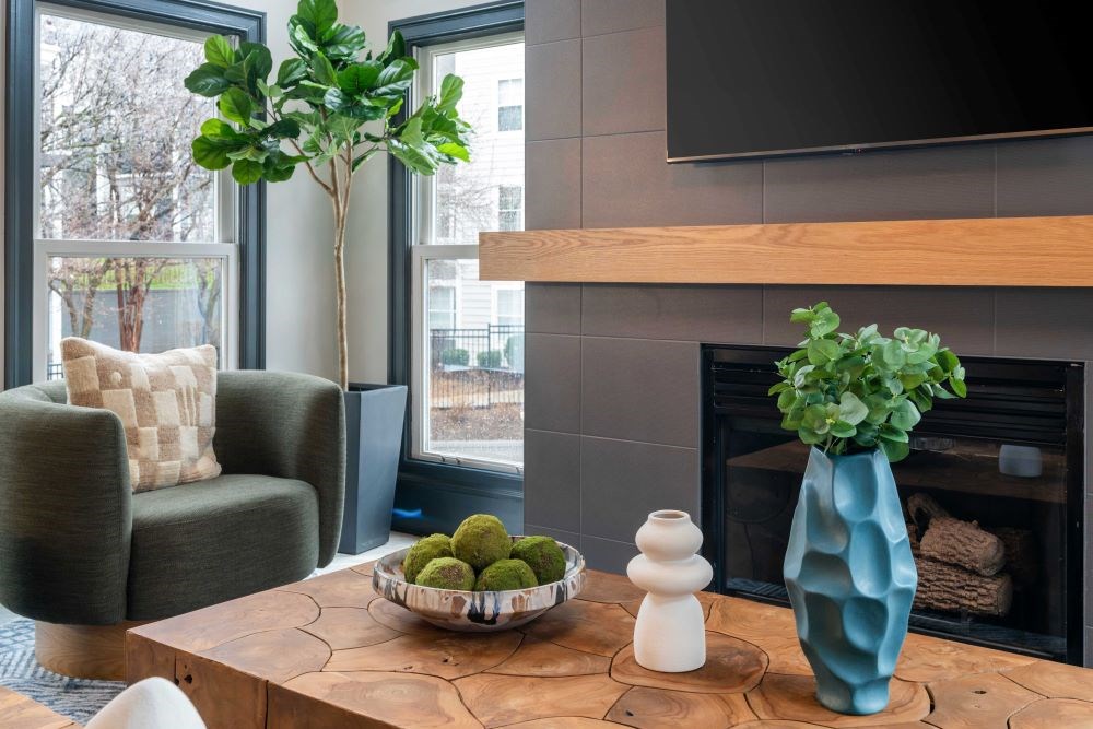 A living room with a fireplace, a chair, a table, and a vase with a plant.
