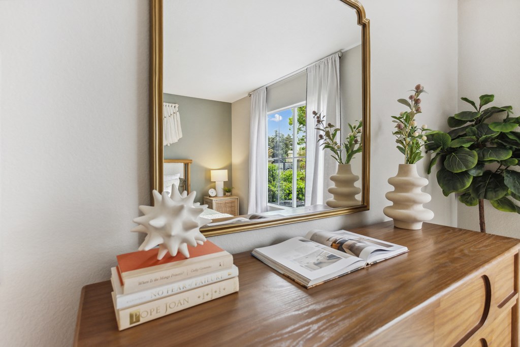 a desk with books and a mirror in a room with a window