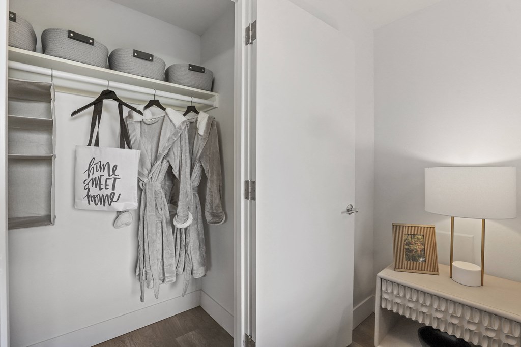 a closet with clothes hanging on a rack in a room with a desk and lamp