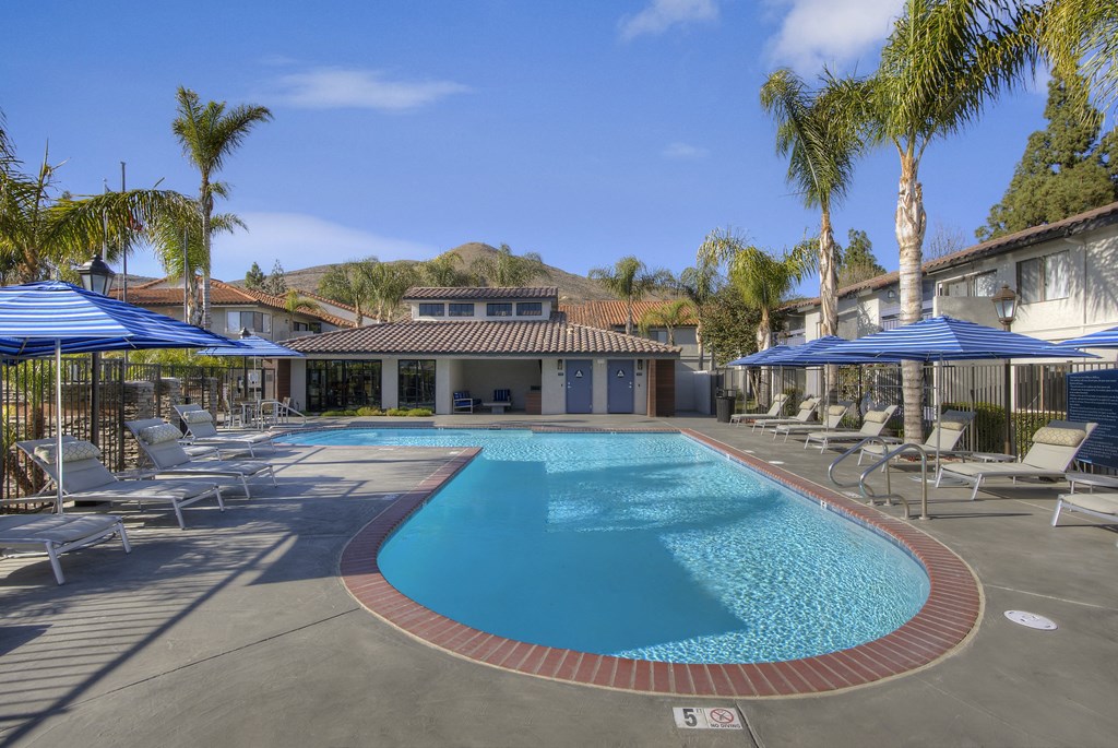 Sofi at Wood Ranch Apartments swimming pool with chairs and umbrellas and a building with palm trees