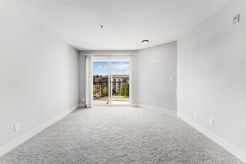 A room with a carpeted floor and a view of a house through a sliding glass door.