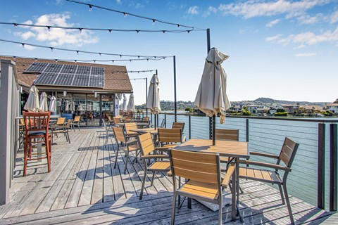 A wooden deck with chairs and tables overlooking a body of water.