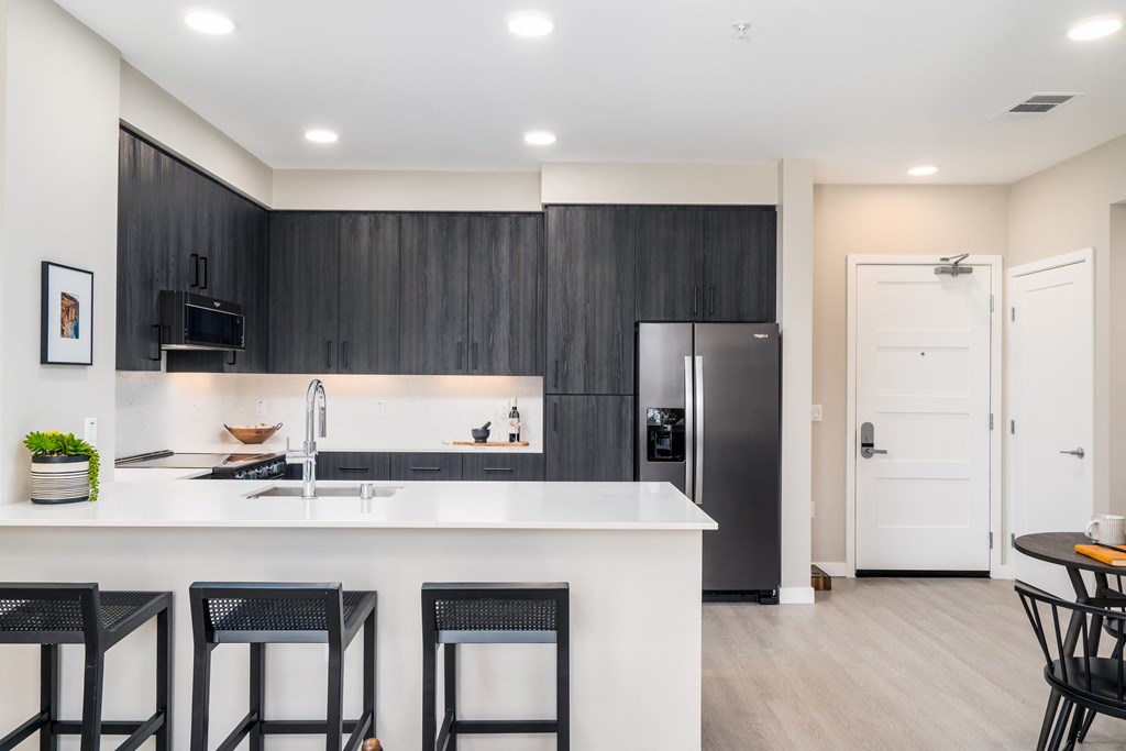a kitchen with a large island with three stools and a refrigerator