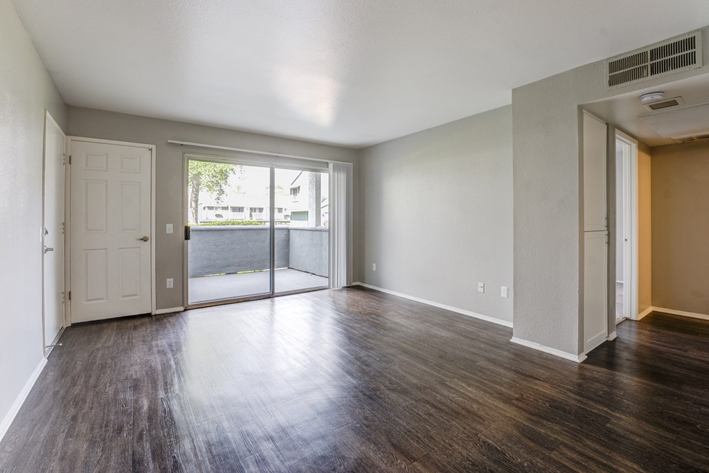 an empty living room with wood floors and a door to a balcony