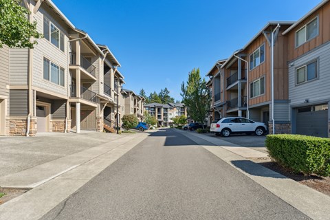 an empty street between two apartment buildings with a white car parked in front