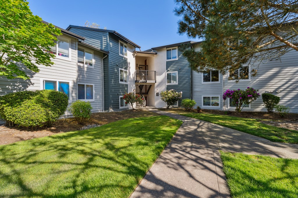 a walkway between two apartment buildings with grass and trees