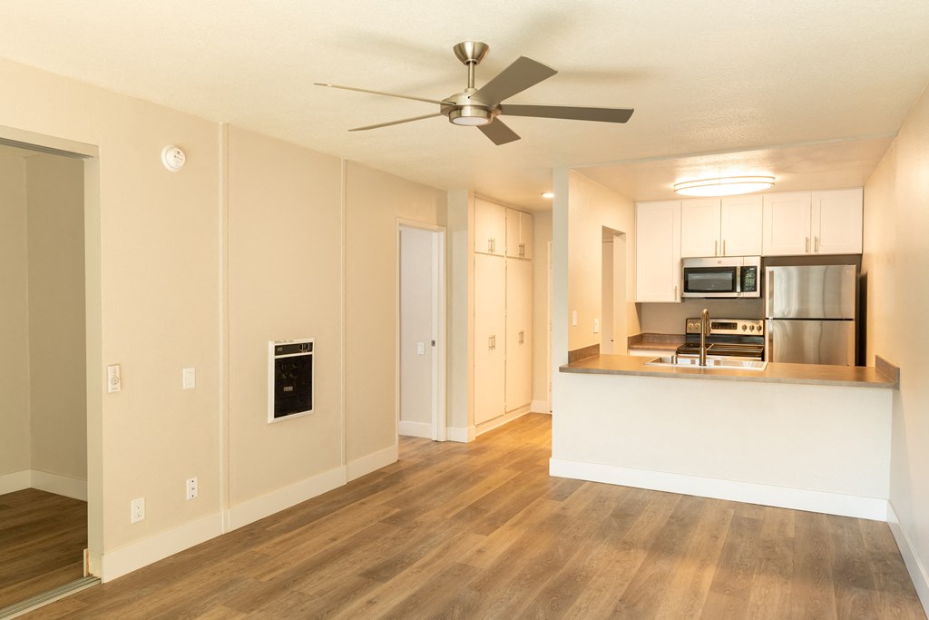 an empty living room with a kitchen and a ceiling fan