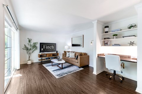 A living room with a couch, a coffee table, and a TV on a wall with the word "Finch" written on it.