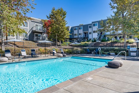 A swimming pool surrounded by chairs and trees.