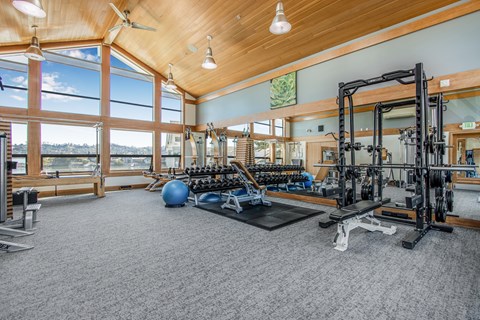A spacious gym with a variety of equipment and a view of the water outside the large windows.
