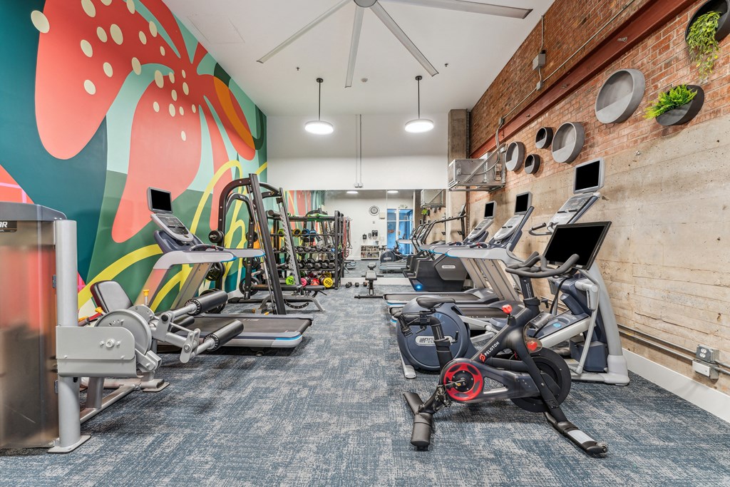 a gym with treadmills and other exercise equipment and a wall with a mural