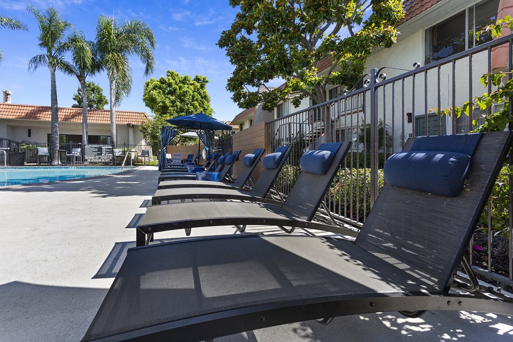 a row of chaise lounges in front of a pool with a building in the