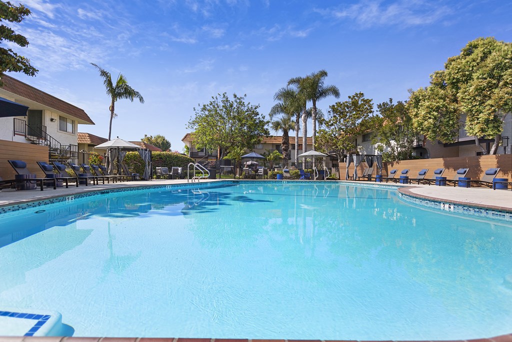 a large swimming pool with lounge chairs and umbrellas in front of a hotel