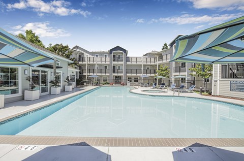 A large swimming pool is surrounded by a white fence and a white building.